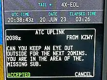 Digital display showing the aircraft registration, the date, the time in UTC "20:38:43z", and the text 'Can you keep an eye out outside for the next 20mins, you are in the area of the missing sub.'