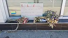 Flowers placed in front of a closed shop. A handwritten sign reads "Hello Loved Customers, We are sad to inform you that we will no longer open for business due to the legislations placed on dispensaries"