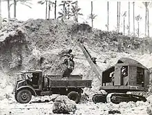 Black and white photo of a mechanical digger dropping soil into the tray of a truck
