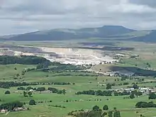 A wide green valley with a large quarry in the middle distance, and a mountain, (Ingleborough) in the background