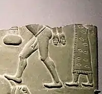 Man in patterned and fringed dress, behind naked prisoner.