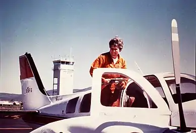 Photo of Mary Barr standing on the wing of her transport plane, 1975