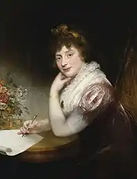Princess Elizabeth rests her left hand on a table. She holds a pen in her right hand, as if she is about to write something.