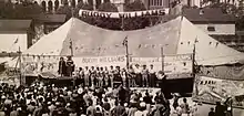 A crowd gathers outside a large tent with banner 'Buddy Williams' between its main poles.