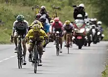 A small group of descending riders led by Julian Alaphilippe wearing a yellow jersey in an extreme tuck position