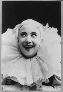 Pilar Morin as clown/mime, in white baldcap and a large white collar: head and shoulders, facing slightly left; smiling