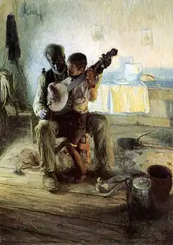A boy holding a banjo seated on an old man's lap